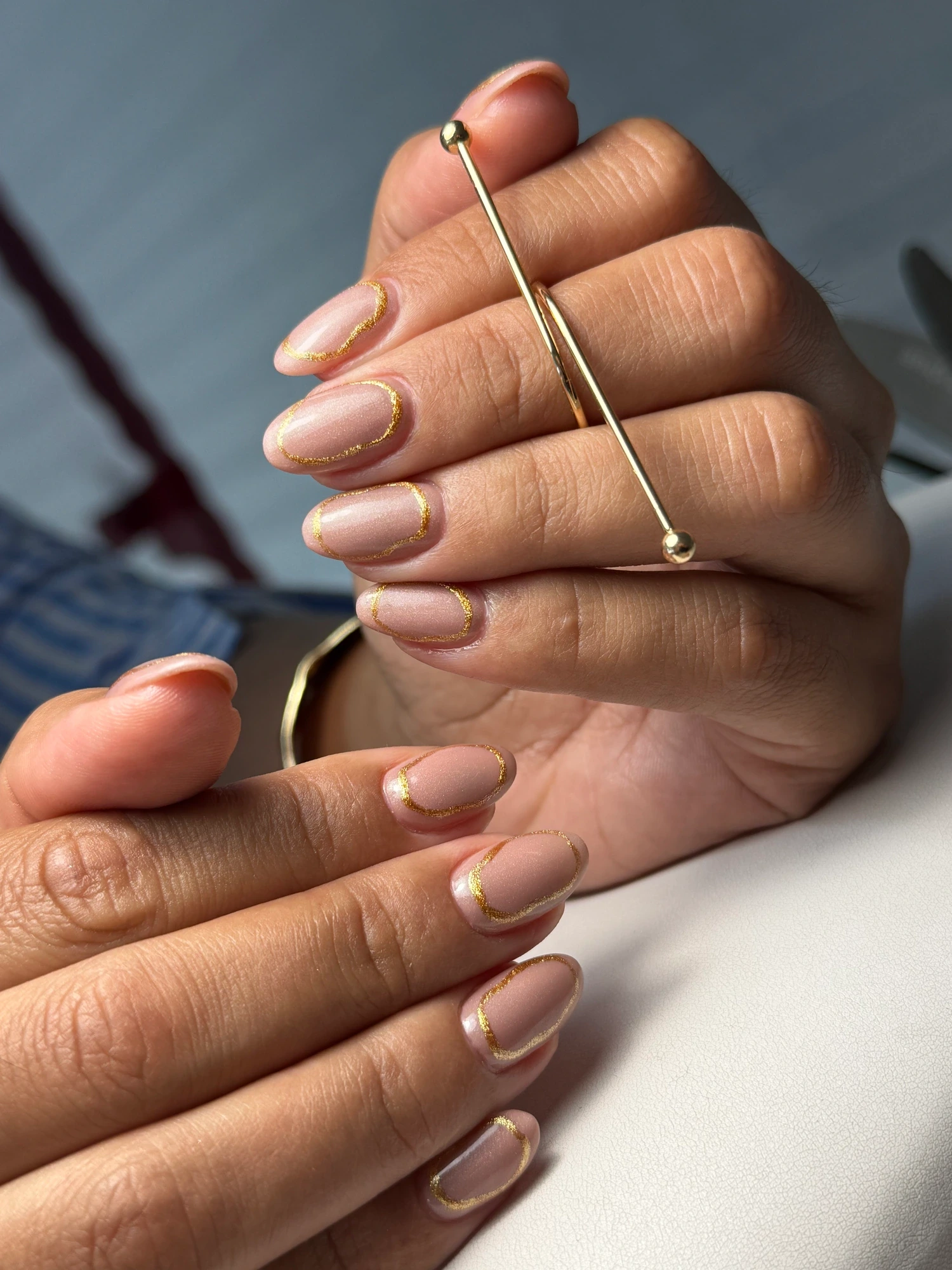 Unhas em tom nude rosado com acabamento brilhante e um anel dourado.