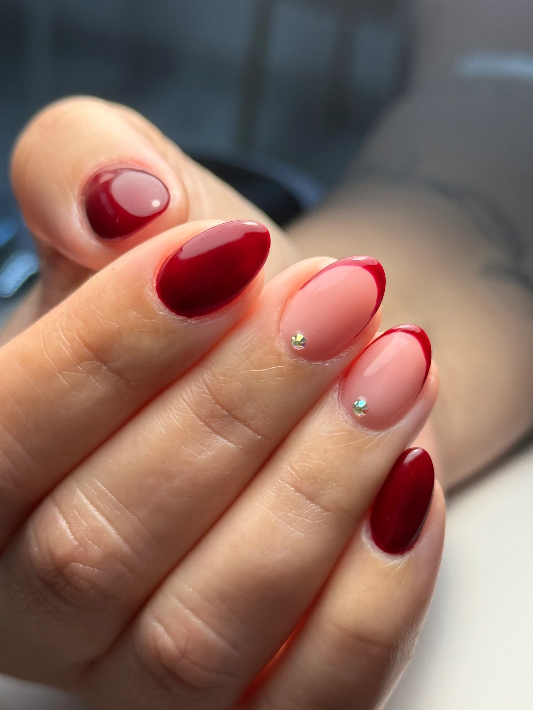 Unhas em vermelho e rosa com pequenos detalhes brilhantes.
